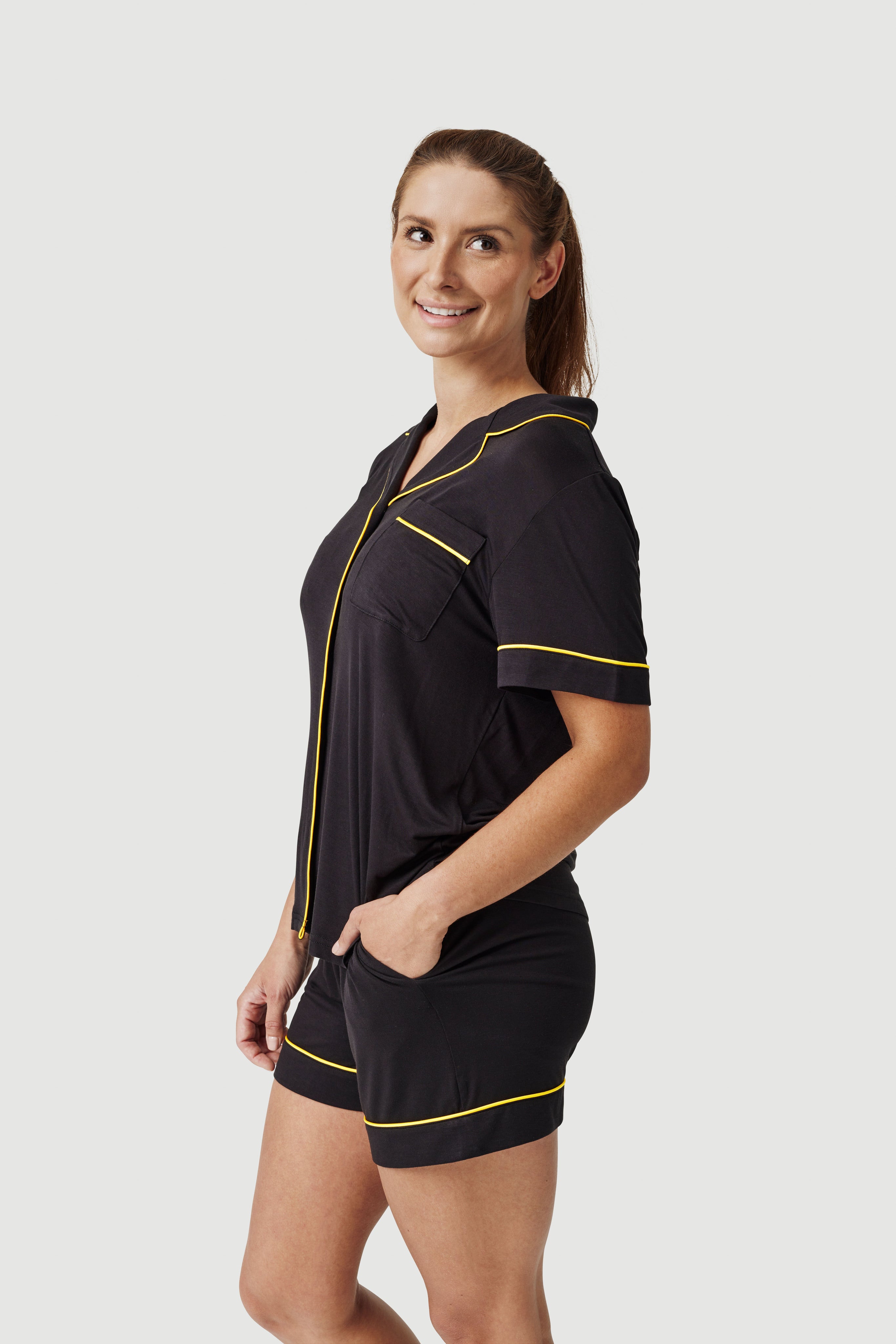 Woman wearing black pajama shorts set with yellow piping, posing against white background