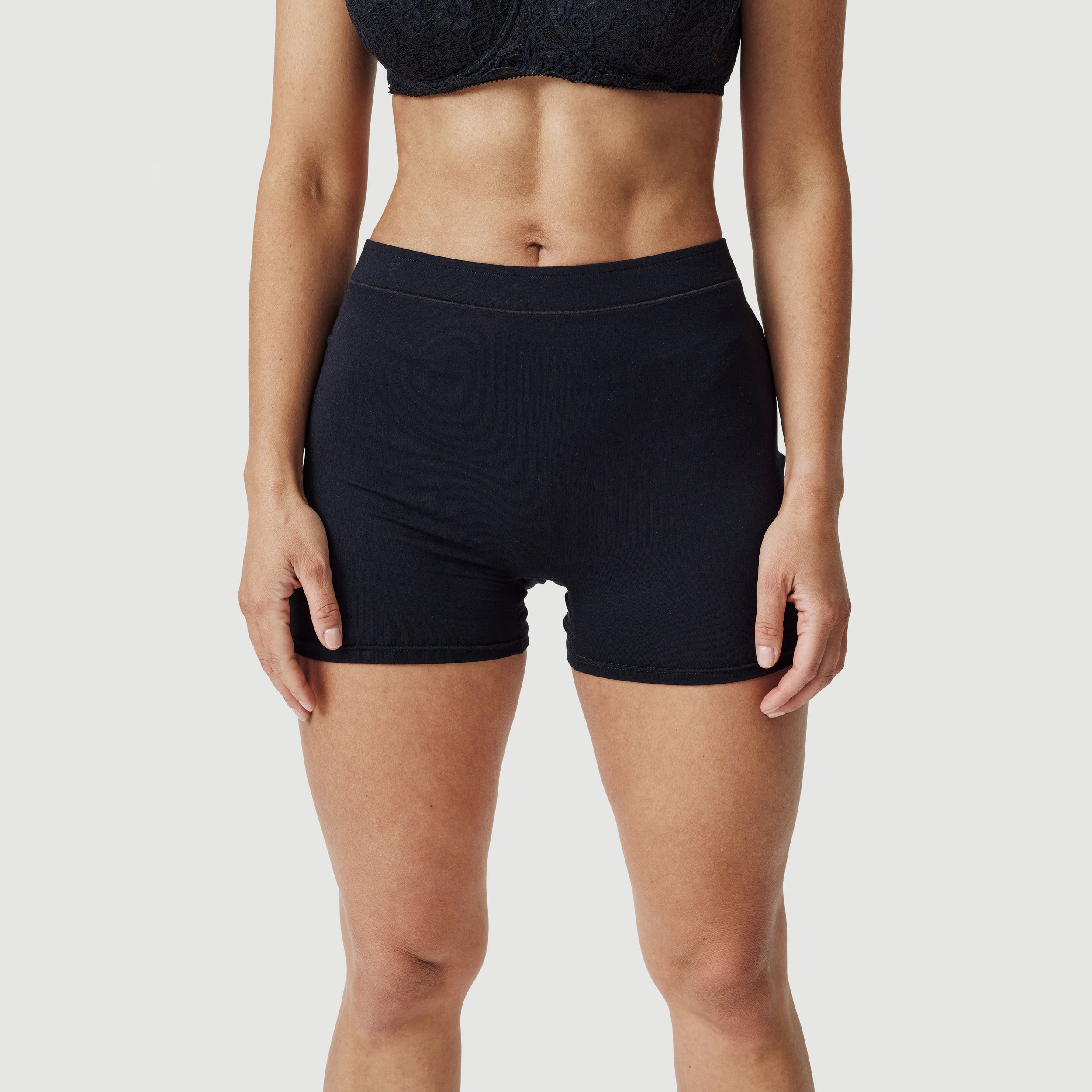 Woman wearing black high-waisted boxer shorts and lace bralette on white background