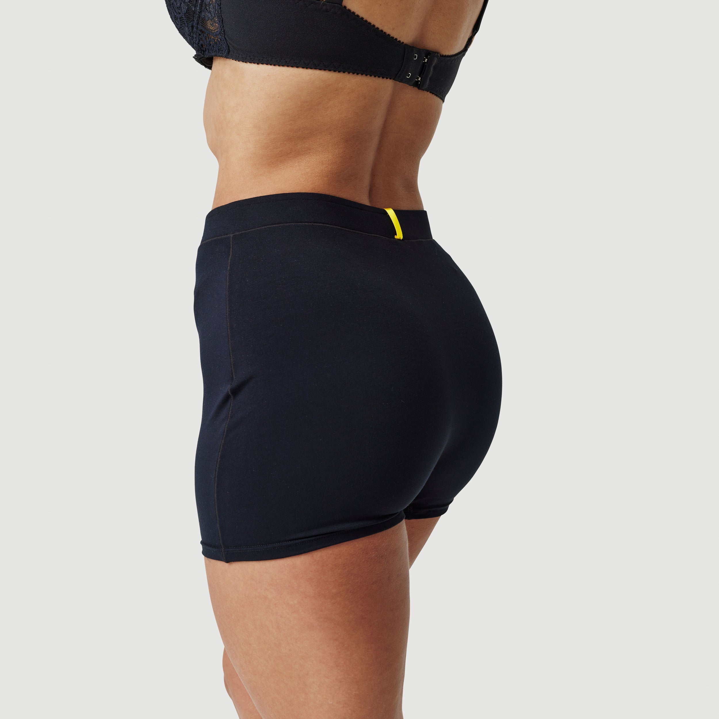 Woman wearing black boxer shorts and bra, side view on plain background, fashion clothing