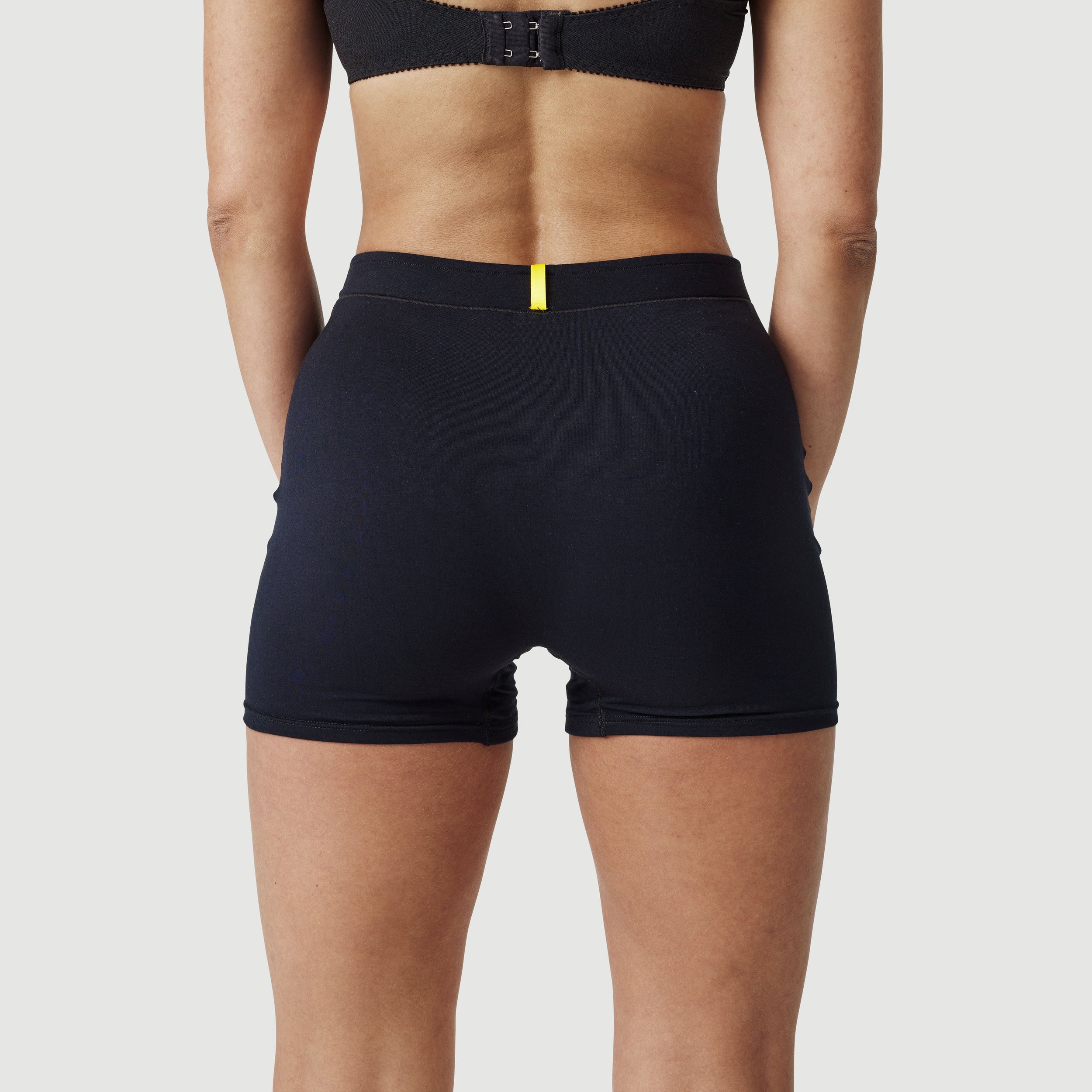 Woman wearing high-waisted black shorts, back view, with yellow accent waistband