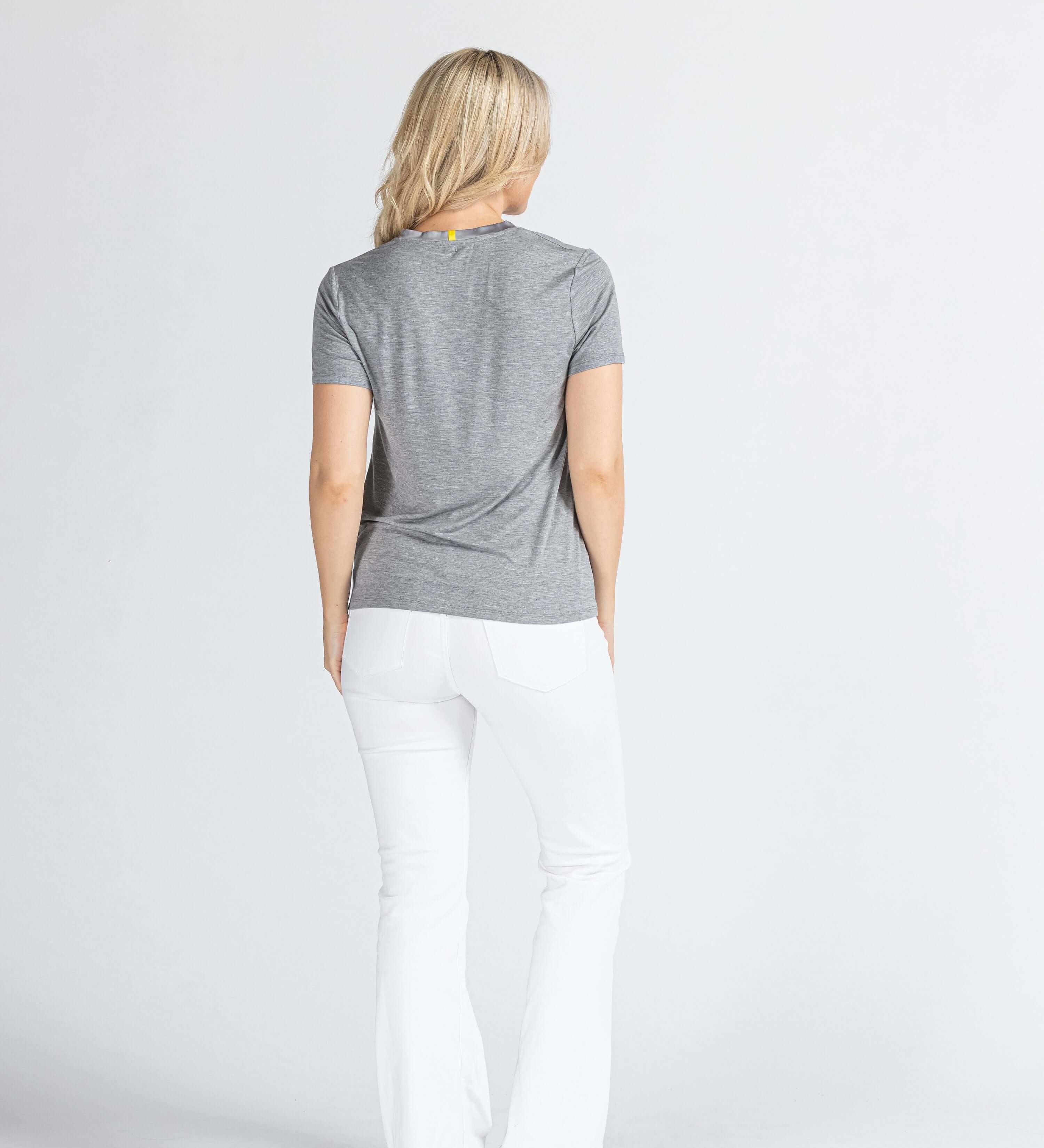 Woman in grey t-shirt and white pants standing against a plain light background