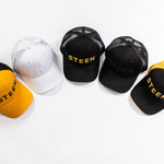 Five STEEN trucker hats in black, white, and yellow mesh on a white background