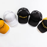 Five STEEN trucker hats in black, white, and yellow mesh on a white background