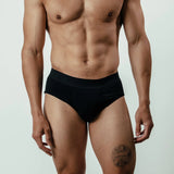 Male model wearing black bamboo briefs, tattoo on thigh, front view against plain background