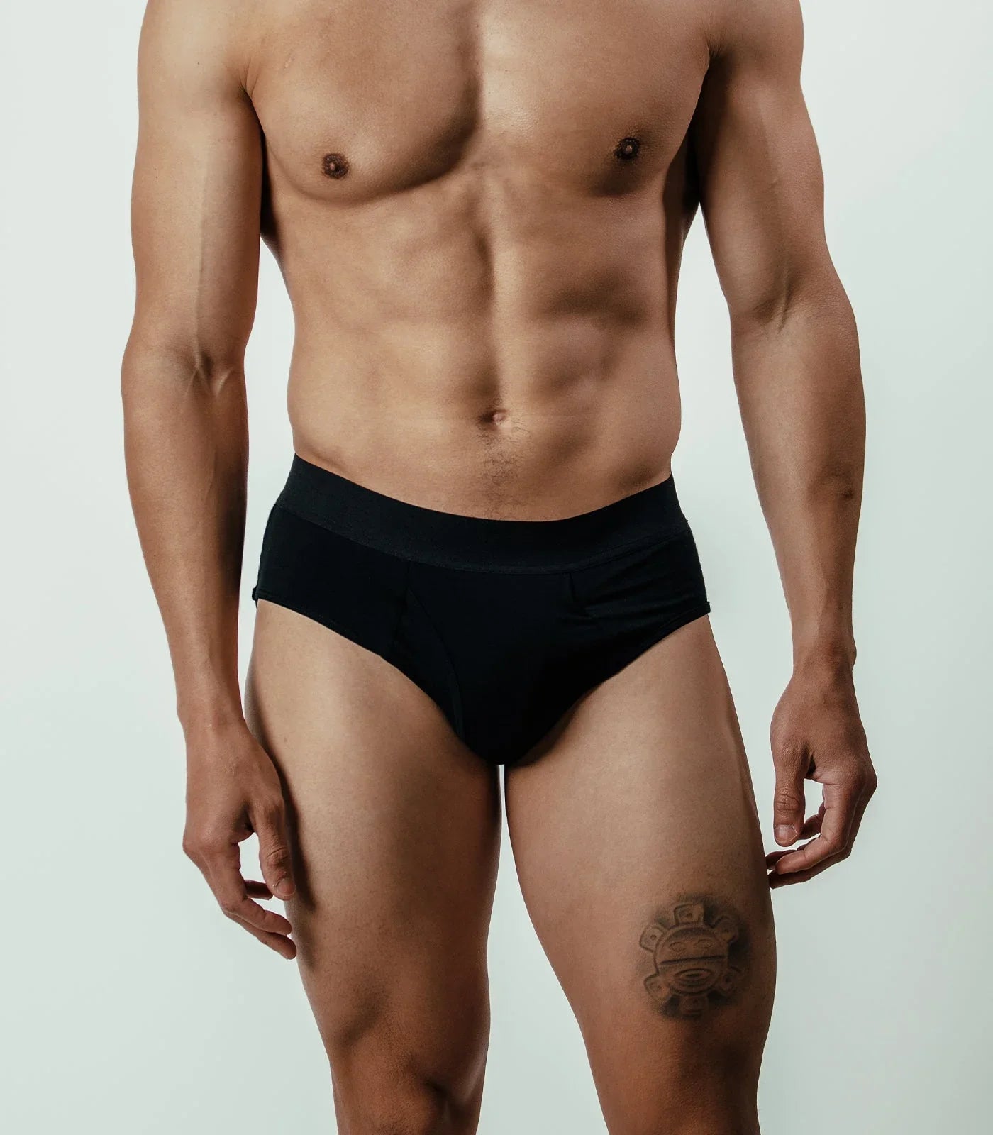 Male model wearing black bamboo briefs, tattoo on thigh, front view against plain background