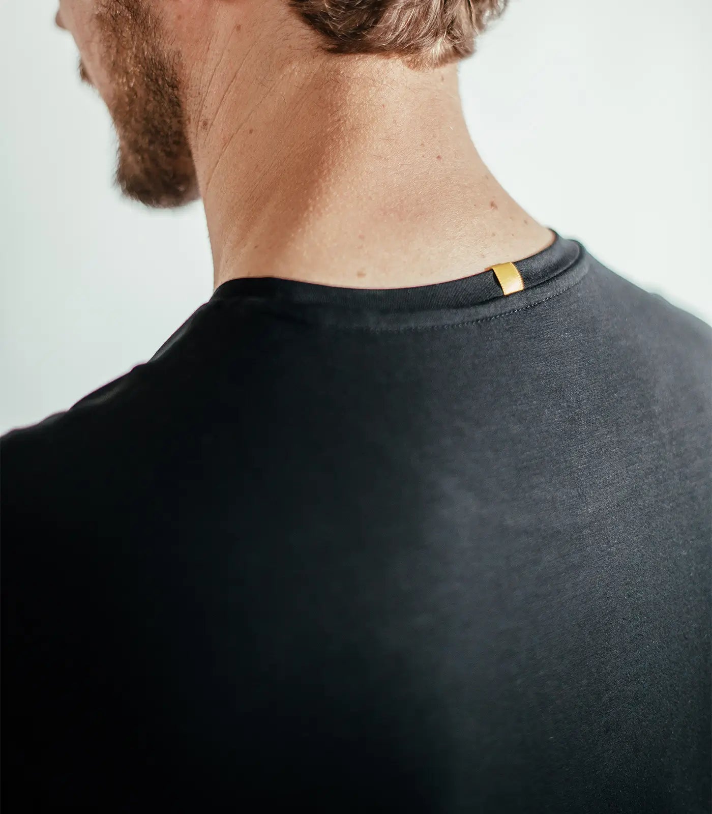 Close-up of man wearing black shirt with yellow tag on neckline, back view